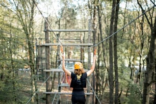 Young well-equipped woman having an active recreation, climbing ropes in the park with obstacles outdoors