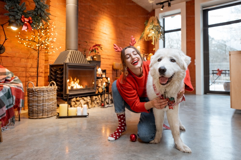Young woman with her cute white dog during a happy New Year holidays sitting by a fireplace at home