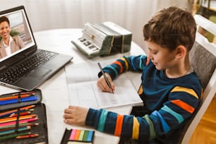 El niño pequeño escribe notas musicales y tecla de violín en casa curso en línea en la computadora portátil. Formación online, clases online.