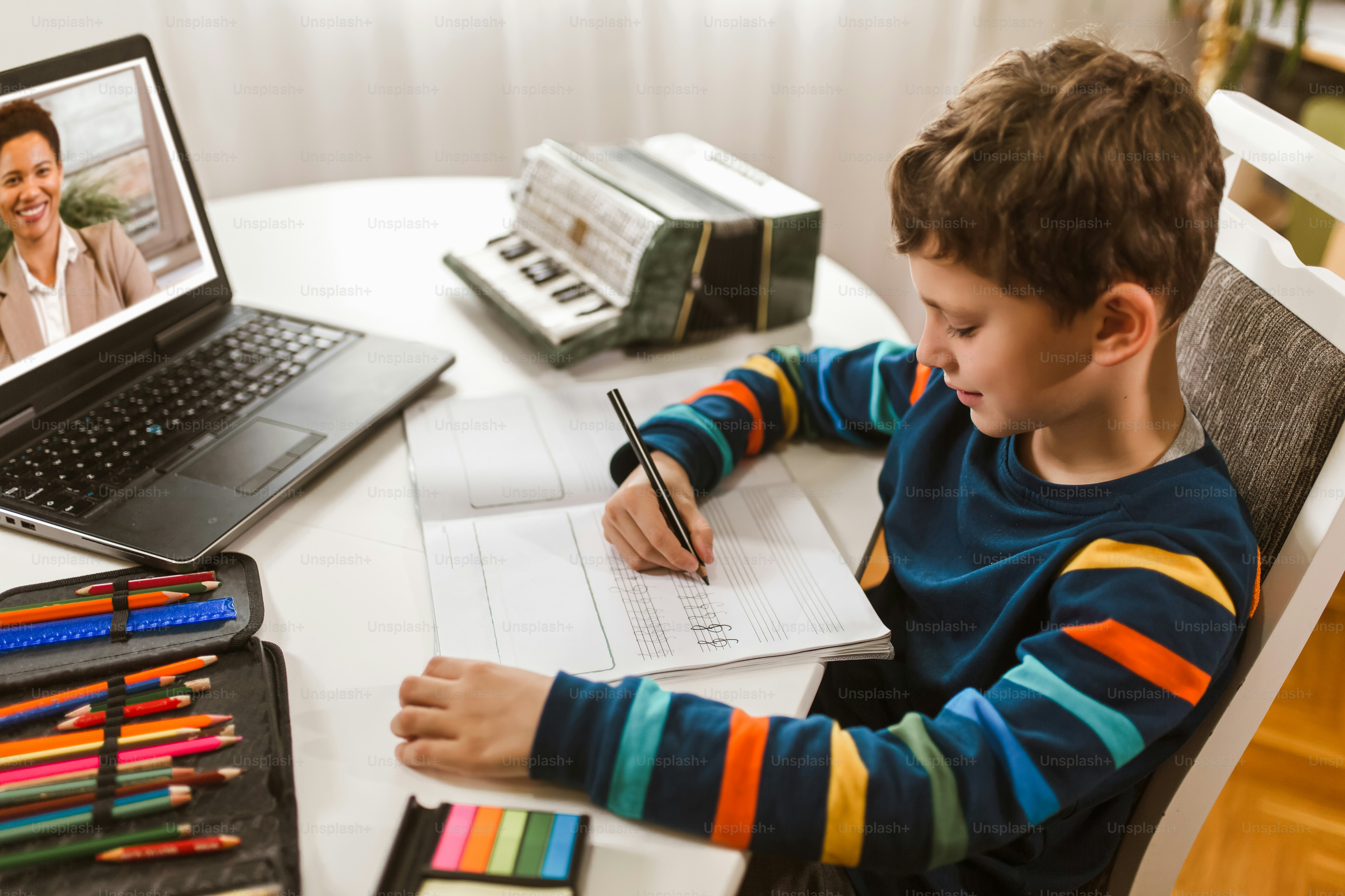 Little boy writes musical notes and violin key at home online course on laptop.Online training, online classes