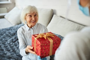 Persona anziana piacevolmente sorpresa che afferra una scatola all'interno di una carta da imballaggio da una donna di assistenza domiciliare