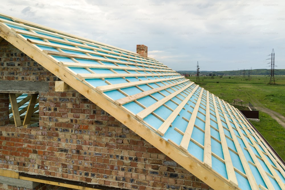 Aerial view of a brick house with wooden roof frame under construction.