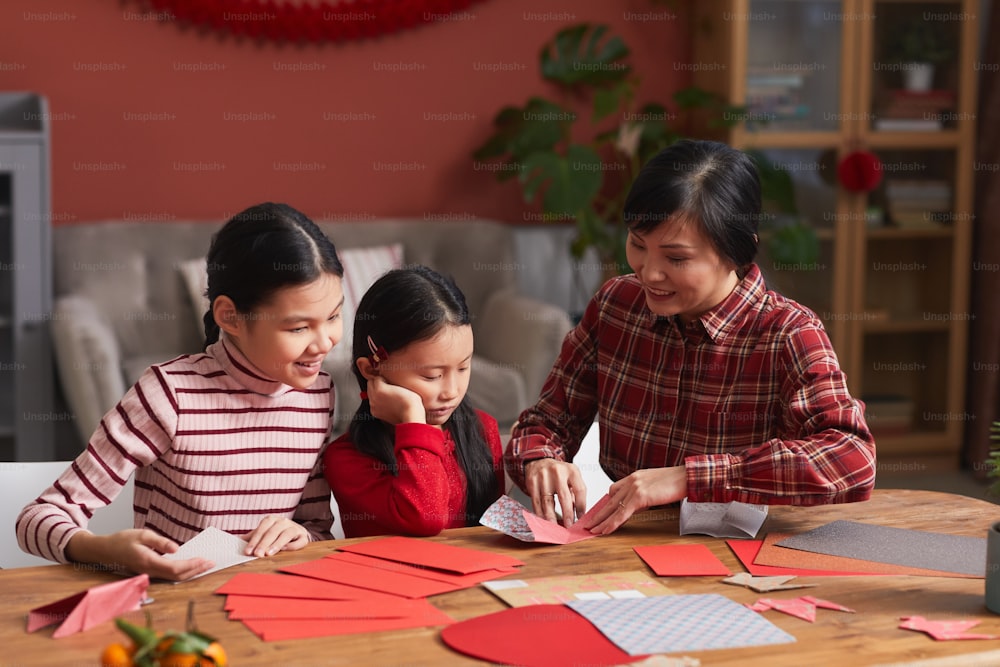 거실에 있는 테이블에 앉아 어린 딸들에게 종이학을 만드는 방법을 보여주는 중국 여성