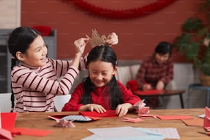 Medium portrait shot of two Chinese girls having fun while preparing colored paper decorations for Lunar New Year holiday