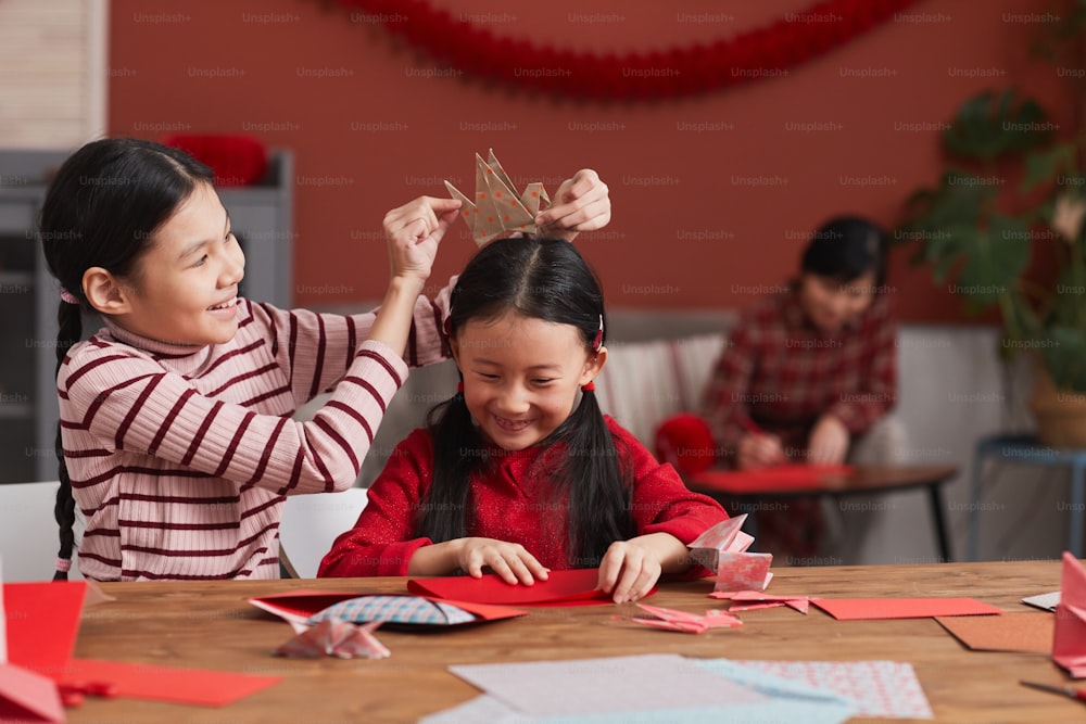 Medium portrait shot of two Chinese girls having fun while preparing colored paper decorations for Lunar New Year holiday