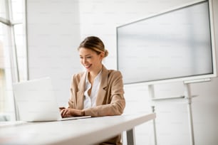 Bella giovane donna che lavora sul computer portatile in un ufficio luminoso con il grande schermo dietro di lei