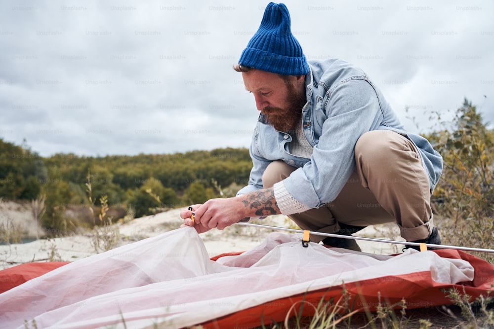 Der gutaussehende bärtige Mann baut in der kalten Jahreszeit ein Zelt für Camping im Freien auf. Reise-, Freiheits-, Lifestyle-Konzept