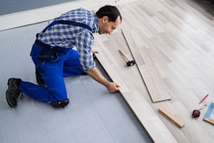 Travailleur installant le plancher de la maison. Charpentier Pose de revêtements de sol stratifiés