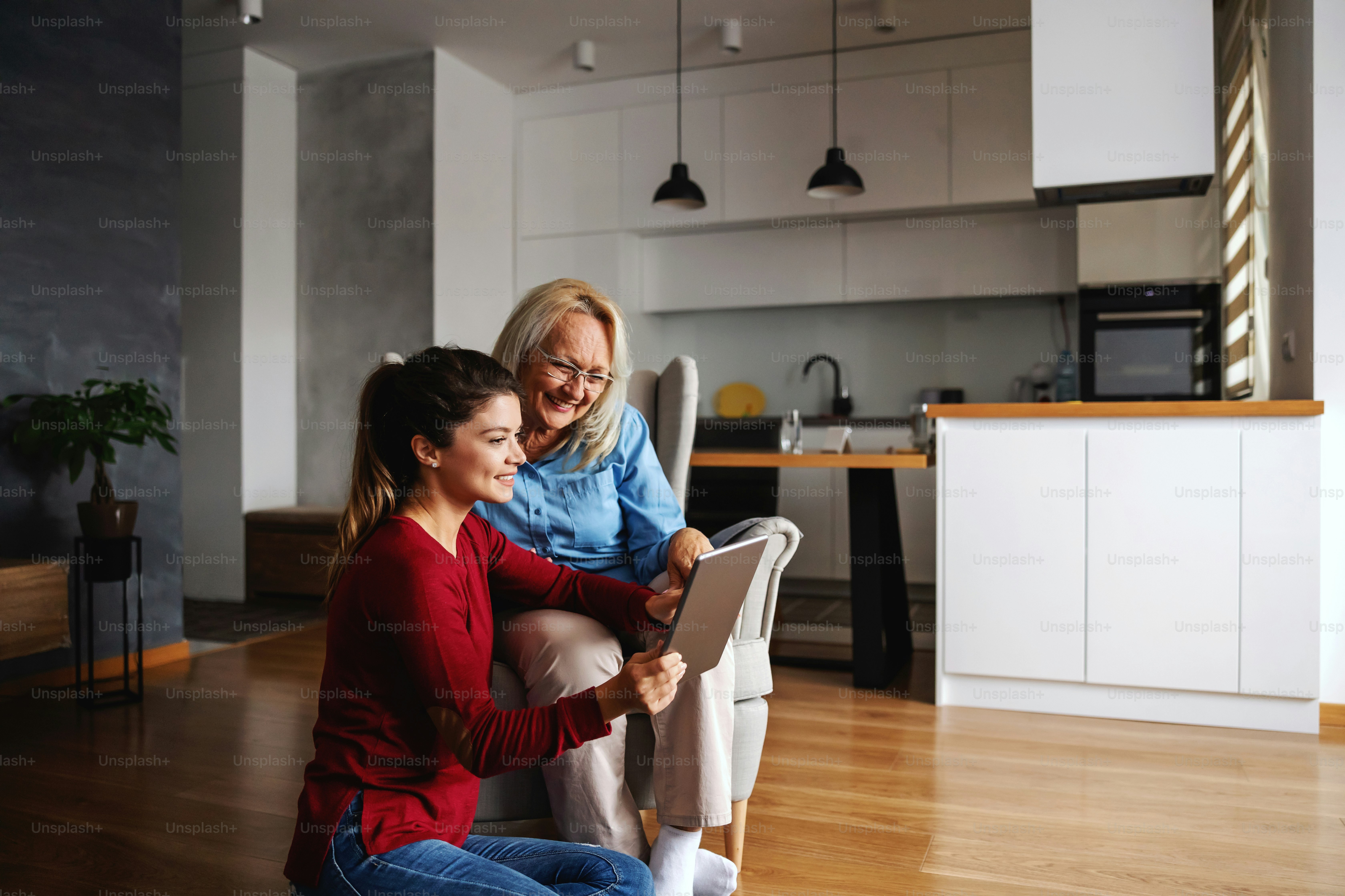 Madre e hija sonrientes sentadas juntas en casa y señalando la tableta ...