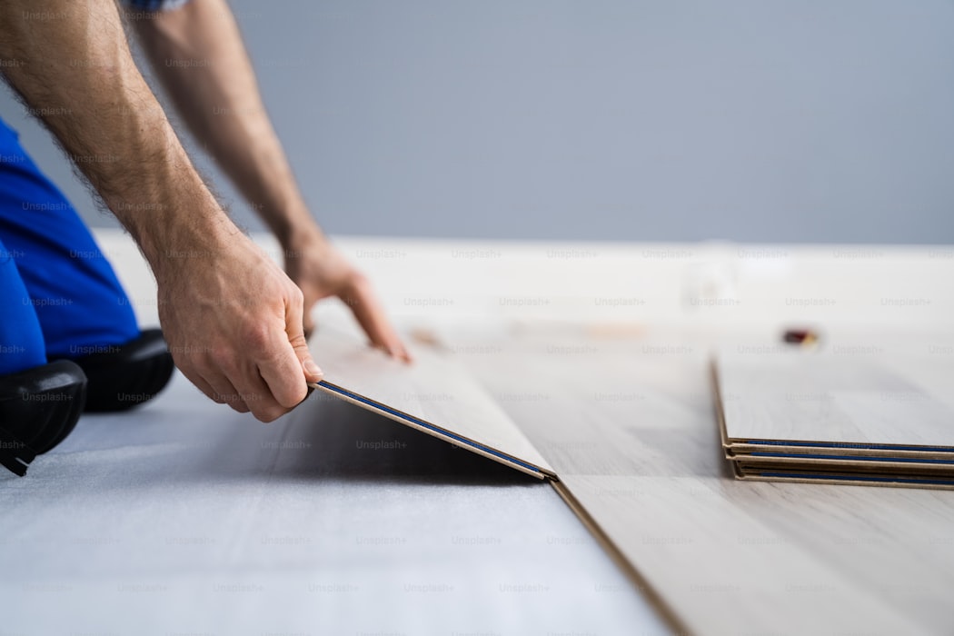 Construction worker installing new laminate flooring on a hardwood subfloor, hands placing a plank, the kind of jobsite scene where contractors use the best estimating app for flooring contractors to quote rooms