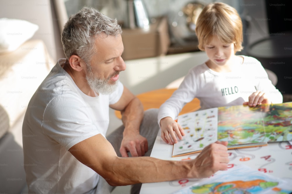 Spending time together. An elderly man and a boy reading a book together