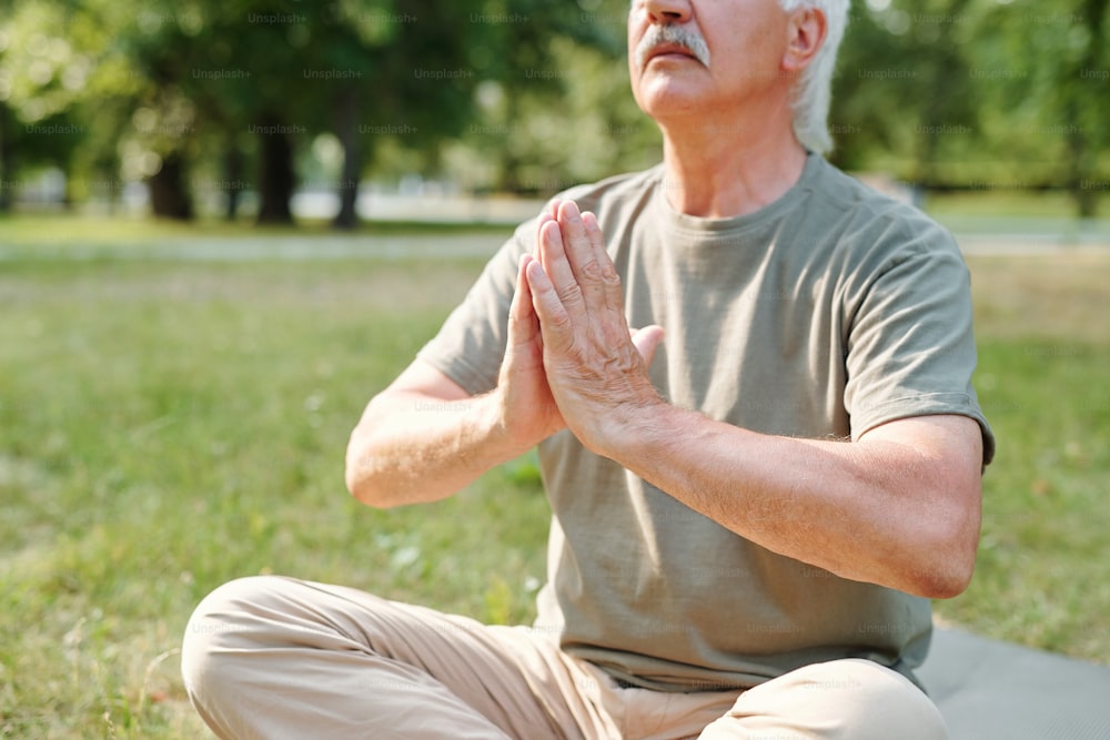 Senior man sitting in lotus position and relaxing during yoga outdoors