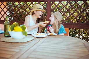 Feliz familia elegante con botella verde de limonada y plato de limones de granja local sentados a la mesa desayunando en la terraza.