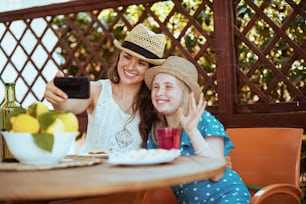 Família moderna sorridente com prato de limões da fazenda local, bate-papo por vídeo em um smartphone e brunch no terraço.
