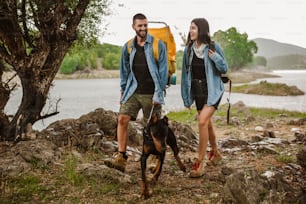 Trek hikers couple and their dog walking in rain trekking on trail trek with backpacks healthy active lifestyle.