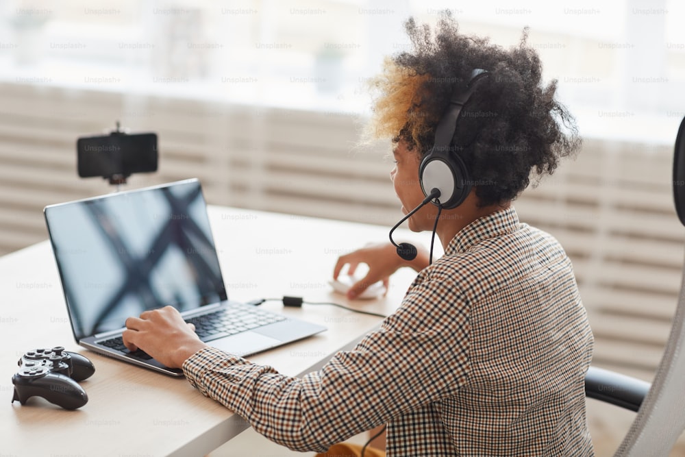 Side view portrait of teenage African-American boy playing video games at home and online streaming, young gamer and blogger concept, copy space