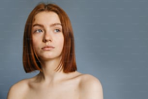 Retrato de perto de uma jovem sem maquiagem com cabelo curto de gengibre e franja lisa, com ombros nus, está olhando para longe enquanto está atrás da câmera