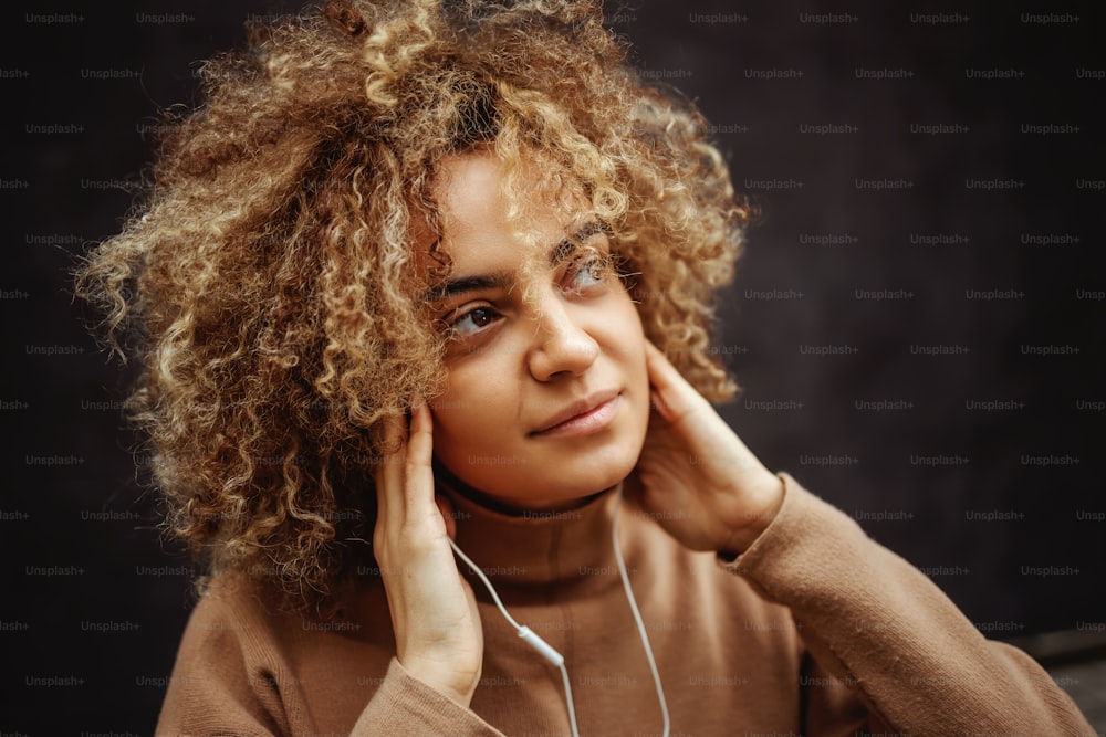 Ragazza con un piccolo sorriso sul viso che tiene le mani sulle orecchie e si gode la musica.