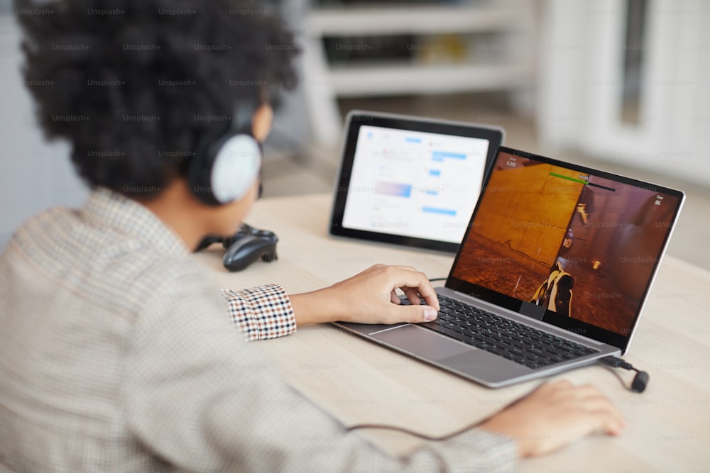 Ritratto di vista laterale del ragazzo afroamericano adolescente che gioca ai videogiochi online tramite laptop, spazio di copia