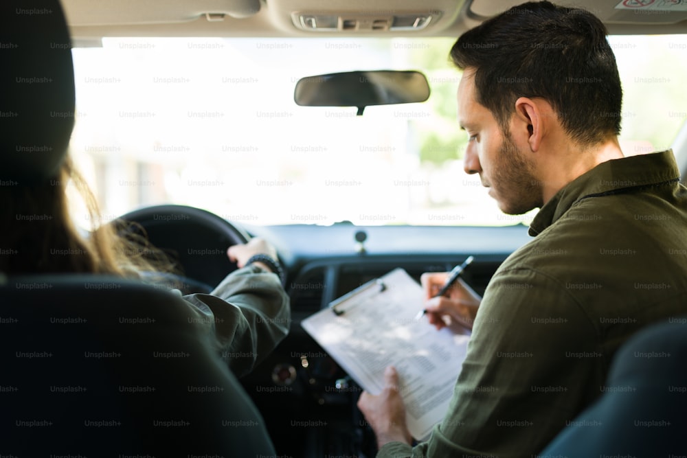 Rear view of an attractive driving school instructor grading the exam of a caucasian adolescent girl during her driving practice