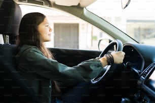 Cheerful teen girl driving her car alone during the day and practicing for her drive test to get her driver's license