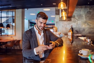 Happy businessman sitting in the bar and using his phone to text a message. Telecommunications, social media