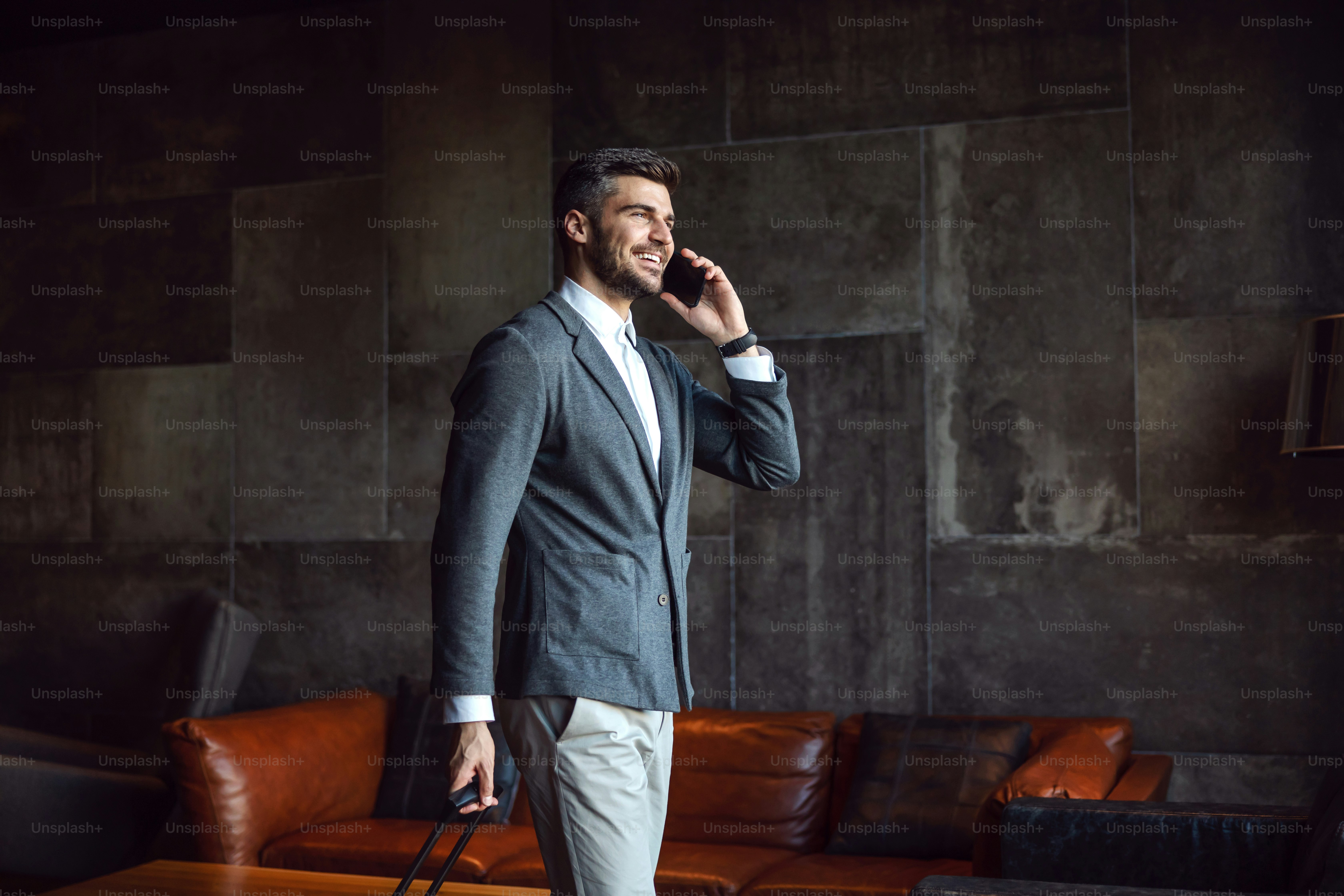 Empresário andando em um corredor de um hotel e recebendo telefonema. Ele está carregando bagagem. Viagem de negócios, tecnologias, telecomunicações