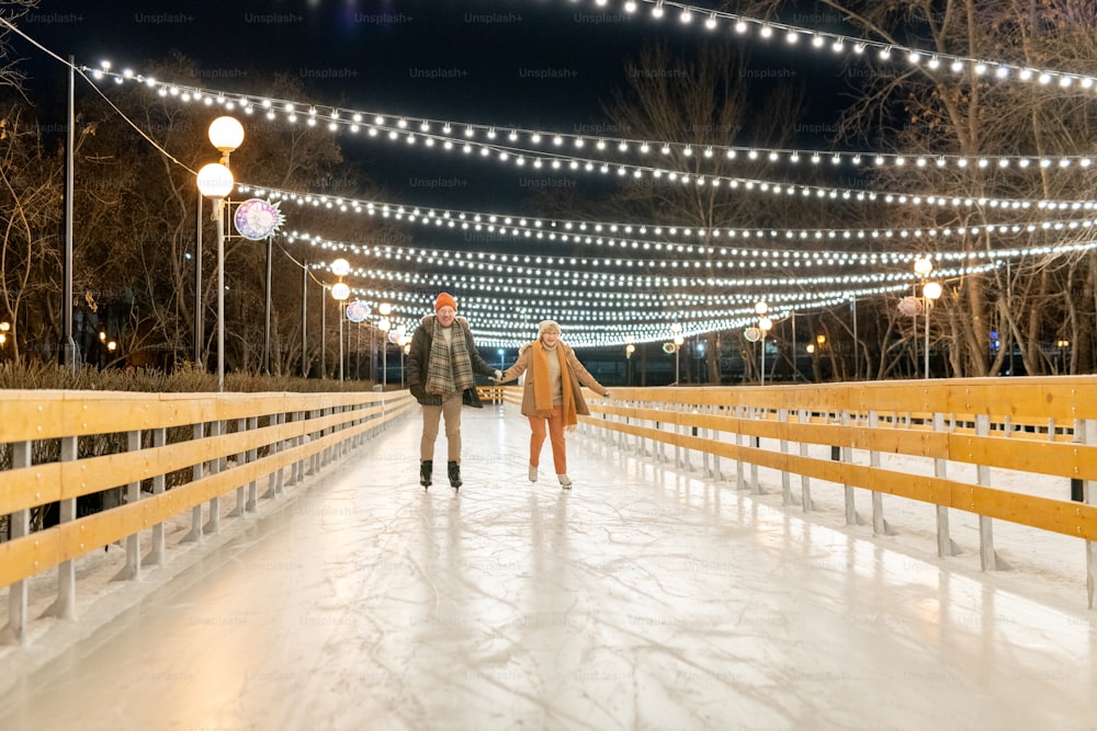Happy mature couple holding hands while skating together on the rink in the park