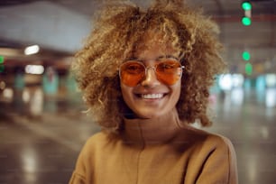 Portrait d’une fille hip-hop métisse souriante avec des lunettes de soleil regardant la caméra.