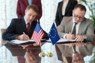 Bandeiras dos Estados Unidos e da União Europeia em cima da mesa contra dois delegados que assinam contrato após negociar e fazer acordo