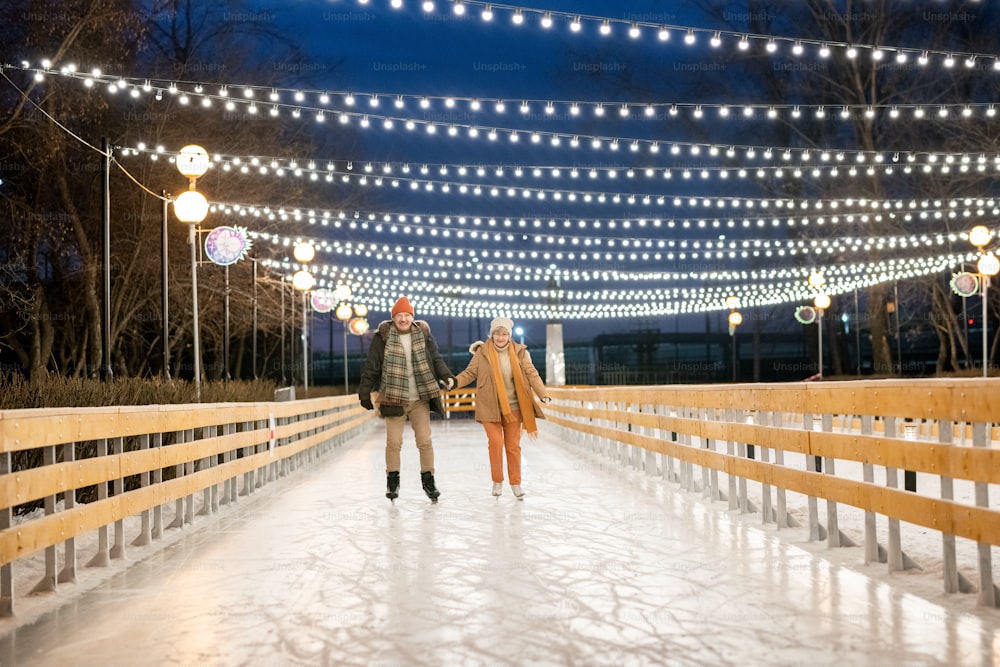 Heureux couple d’âge mûr se tenant la main sur la patinoire dans le parc