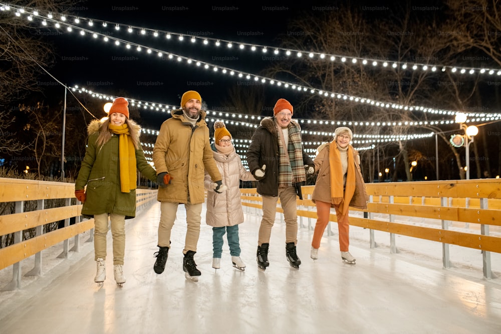 Große, glückliche Familie, die in den Weihnachtsferien auf der Eisbahn reitet