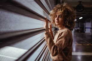 Serious mixed race trap girl standing next to garage door and looking at camera.