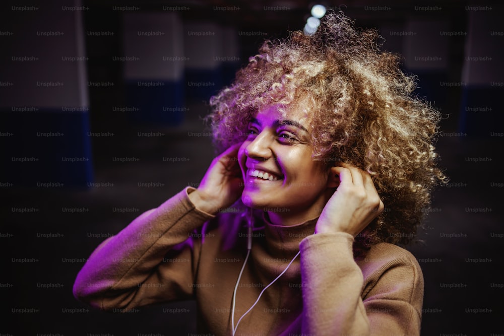 Sonriente chica de hip hop de raza mixta parada en un garaje subterráneo y disfrutando de la música.