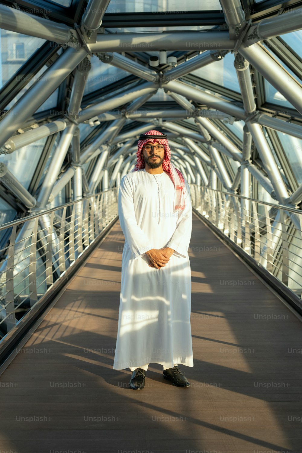Junger selbstbewusster Geschäftsmann oder Delegierter in arabischer Nationalkleidung, der vor der Kamera auf einem langen Gang im Business Center steht
