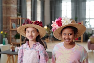 Portrait of two little girls in beautiful hats with flowers smiling at camera