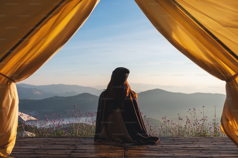 Immagine posteriore di una donna seduta sul balcone di legno mentre guarda una bellissima vista sulle montagne e sulla natura fuori dalla tenda