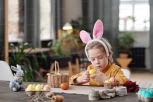 Little boy in rabbit ears sitting at the table and preparing for Easter holiday
