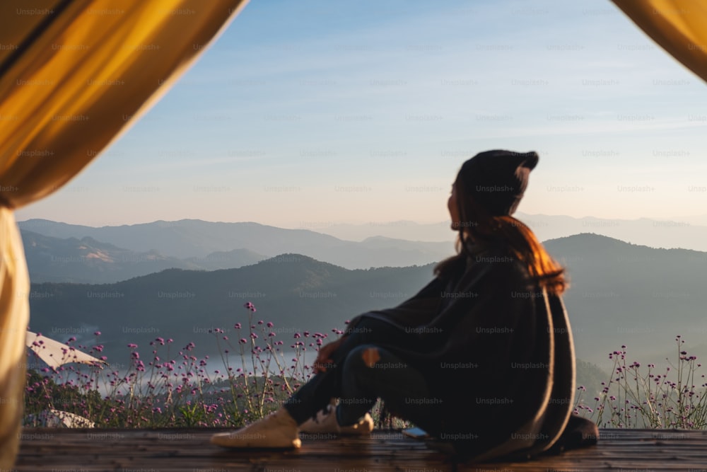 テントの外の美しい山々と自然の景色を見ながら木製のバルコニーに座っている女性の背面図画像