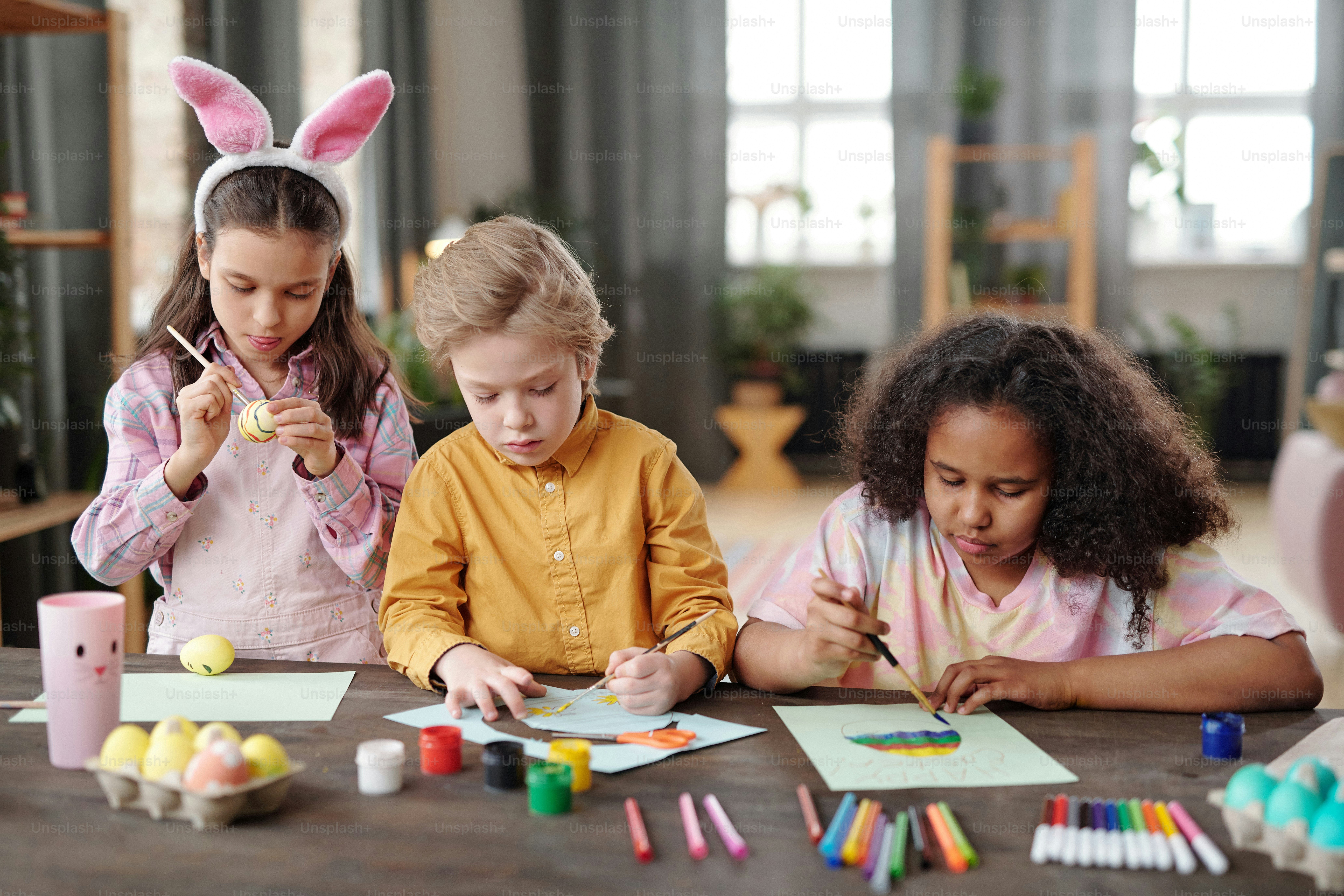 Group of children sitting at the table with paints and paintbrushes and painting pictures at art class