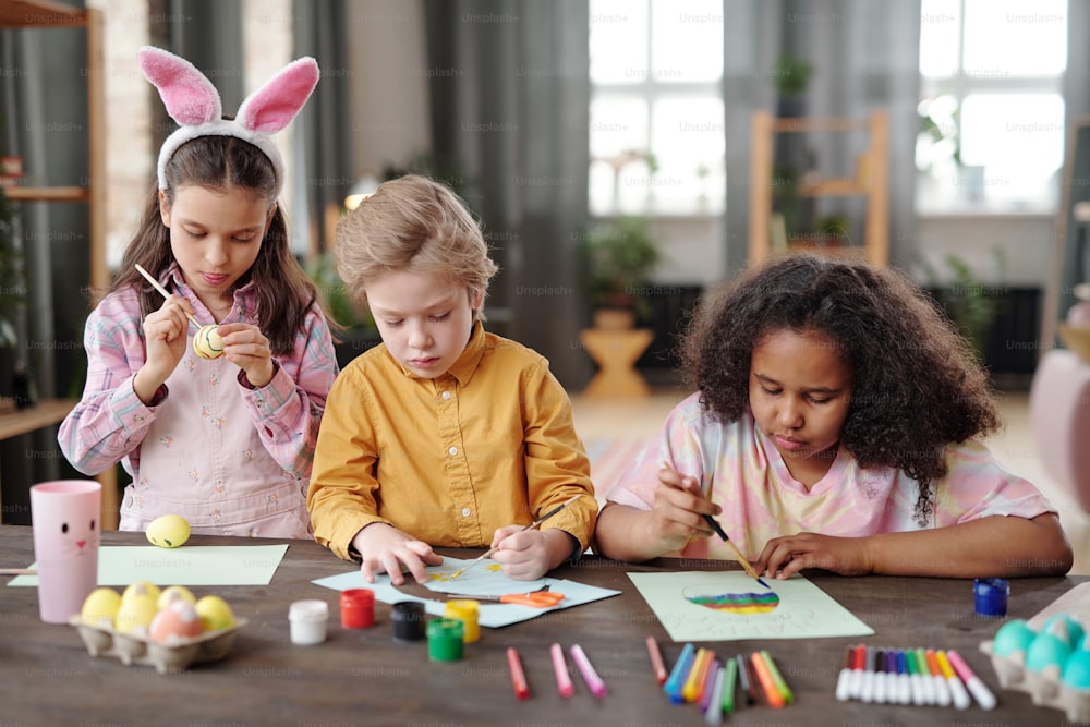 Gruppe von Kindern, die mit Farben und Pinseln am Tisch sitzen und Bilder im Kunstunterricht malen