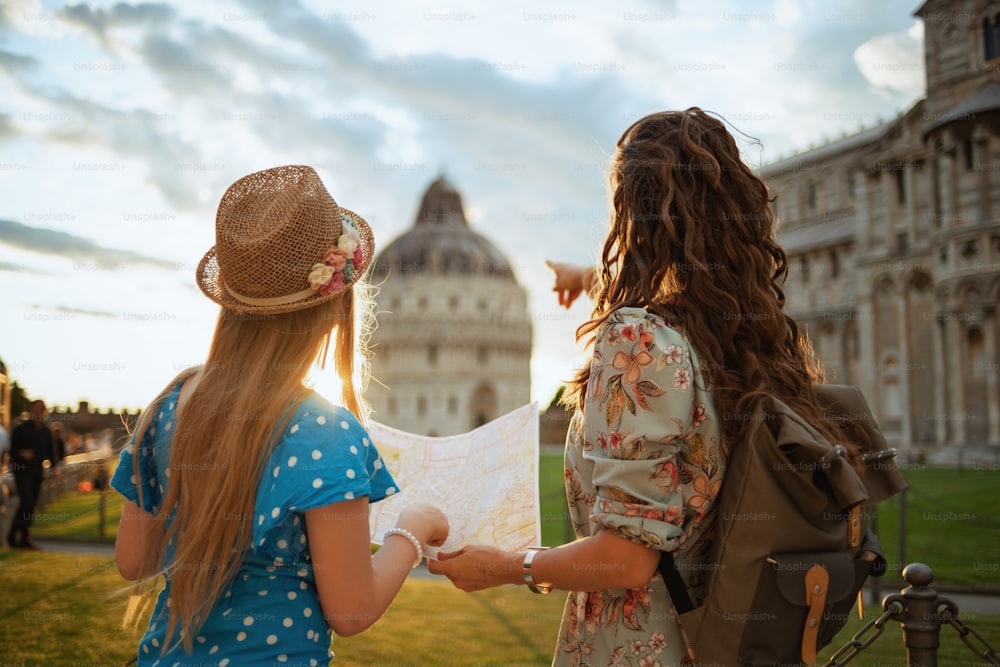 Visto da dietro madre e bambino alla moda con mappa e zaino turistico vicino al Duomo di Pisa.