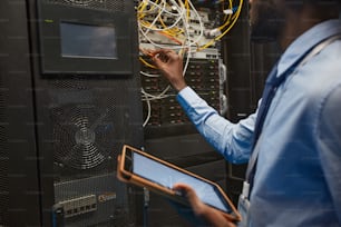 아프리카계 미국인 네트워크 엔지니어가 데이터 센터에서 슈퍼컴퓨터로 작업하는 동안 서버 캐비닛에 케이블을 연결하는 자르기 초상화, 복사 공간