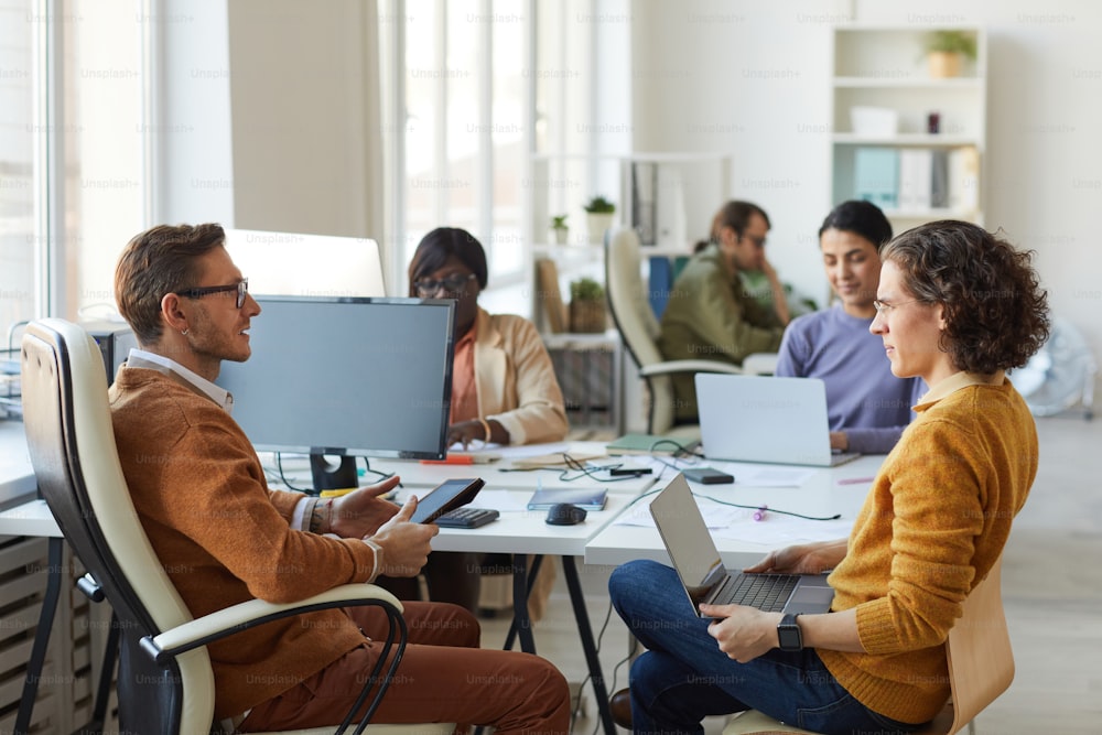 Side view portrait of young business team discussing project while working at desk in white office interior, copy space