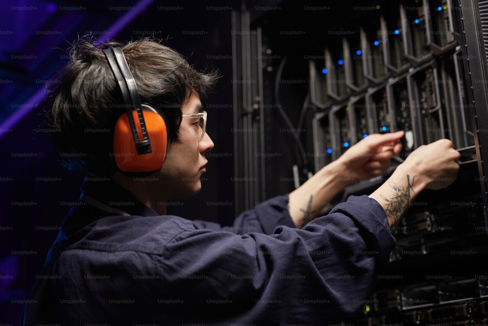 Retrato da vista lateral do jovem engenheiro de rede tatuado configurando servidores no centro de dados do supercomputador, espaço de cópia