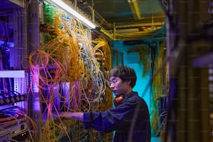 Retrato da vista lateral do jovem técnico de rede conectando cabos na sala do servidor, espaço de cópia
