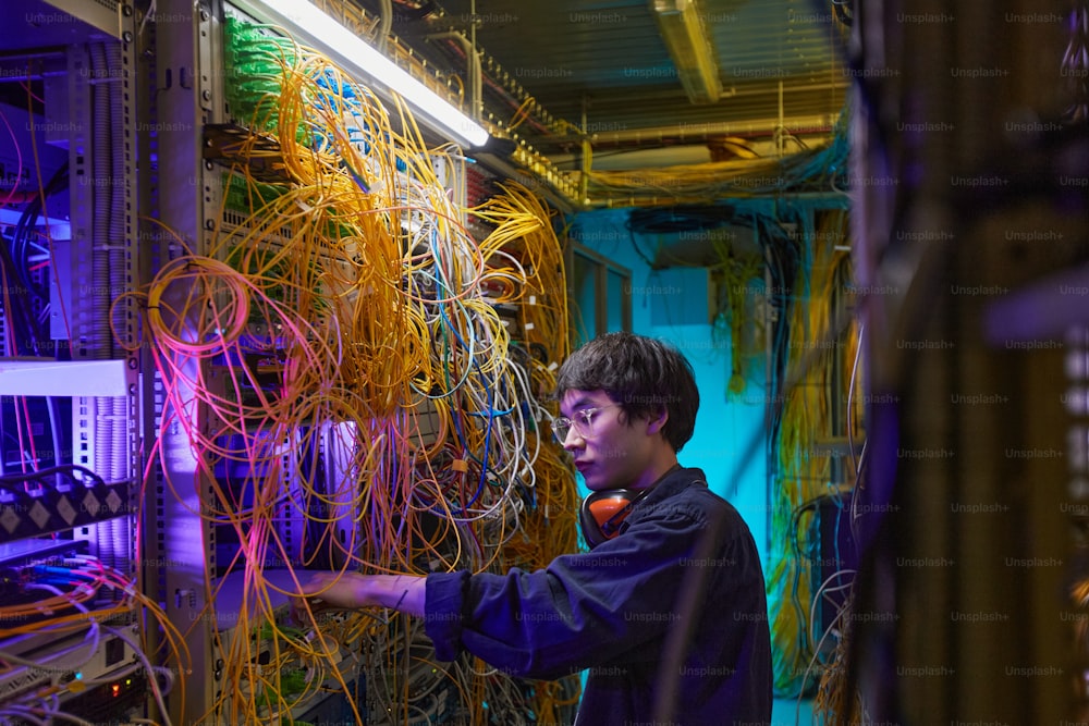 Vista lateral Retrato de un joven técnico de red que conecta cables en la sala de servidores, espacio de copia