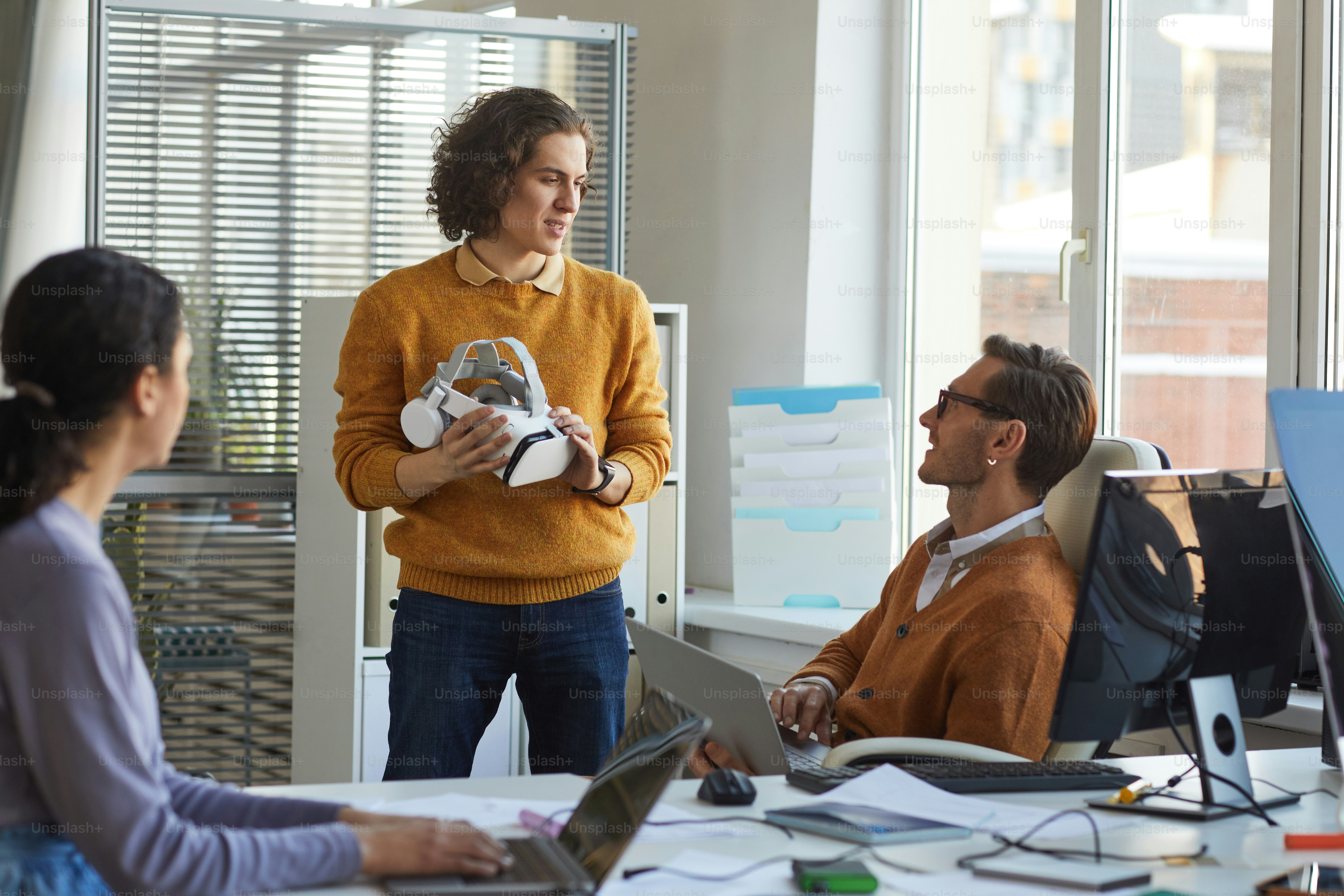 Porträt eines jungen IT-Entwicklers, der ein VR-Headset in der Hand hält, während er mit dem Team im Software-Produktionsstudio, Copy Space, arbeitet
