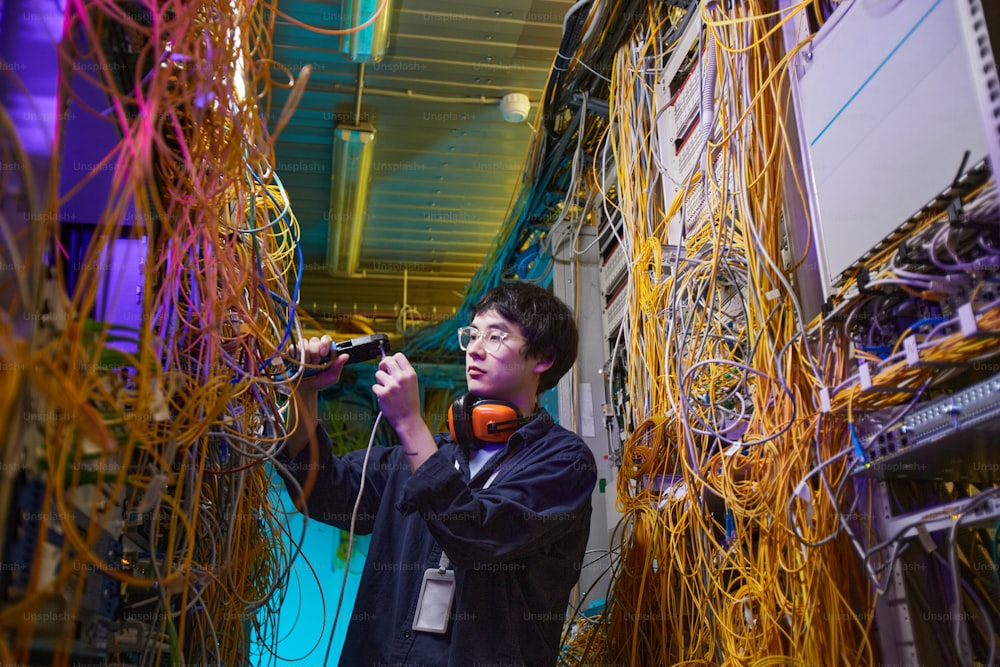Retrato de cintura para arriba del joven técnico de red que conecta cables en la sala de servidores, espacio de copia