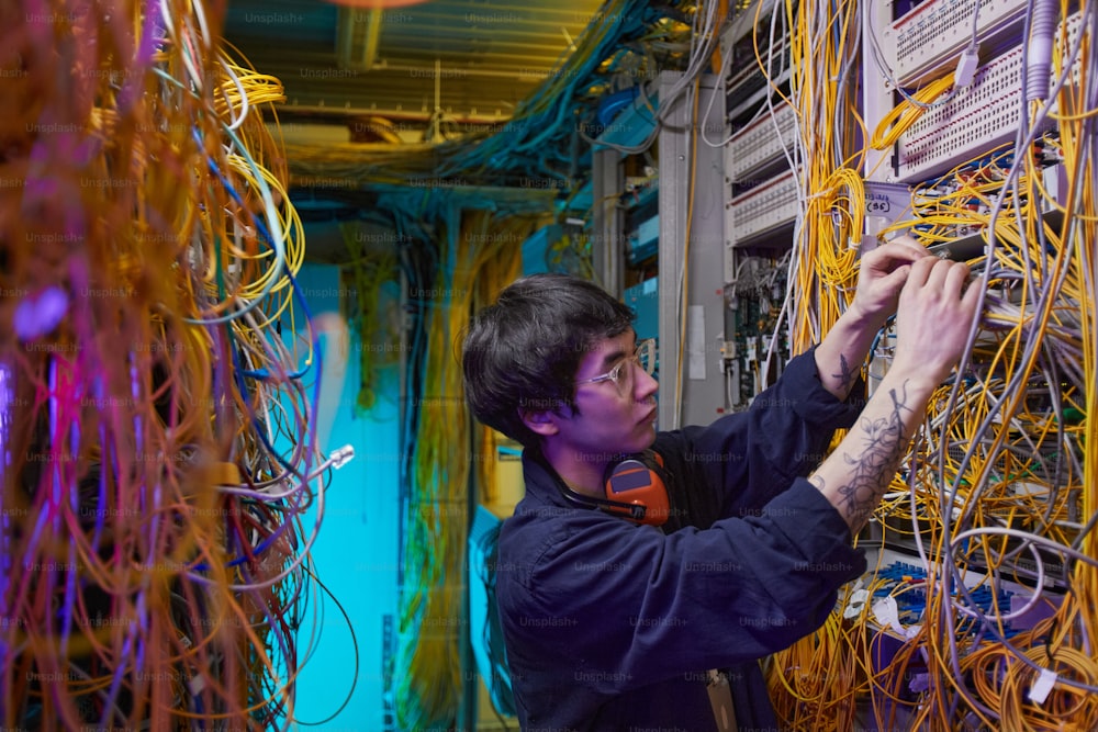 Vista lateral retrato de un joven técnico de redes que conecta alambres y cables en la sala de servidores, espacio de copia